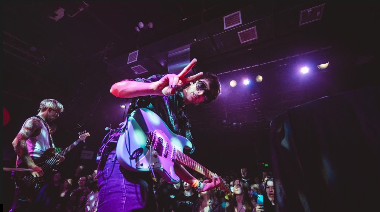 Dan Smith from Nightbreakers posing on stage at a concert with purple overlay. 