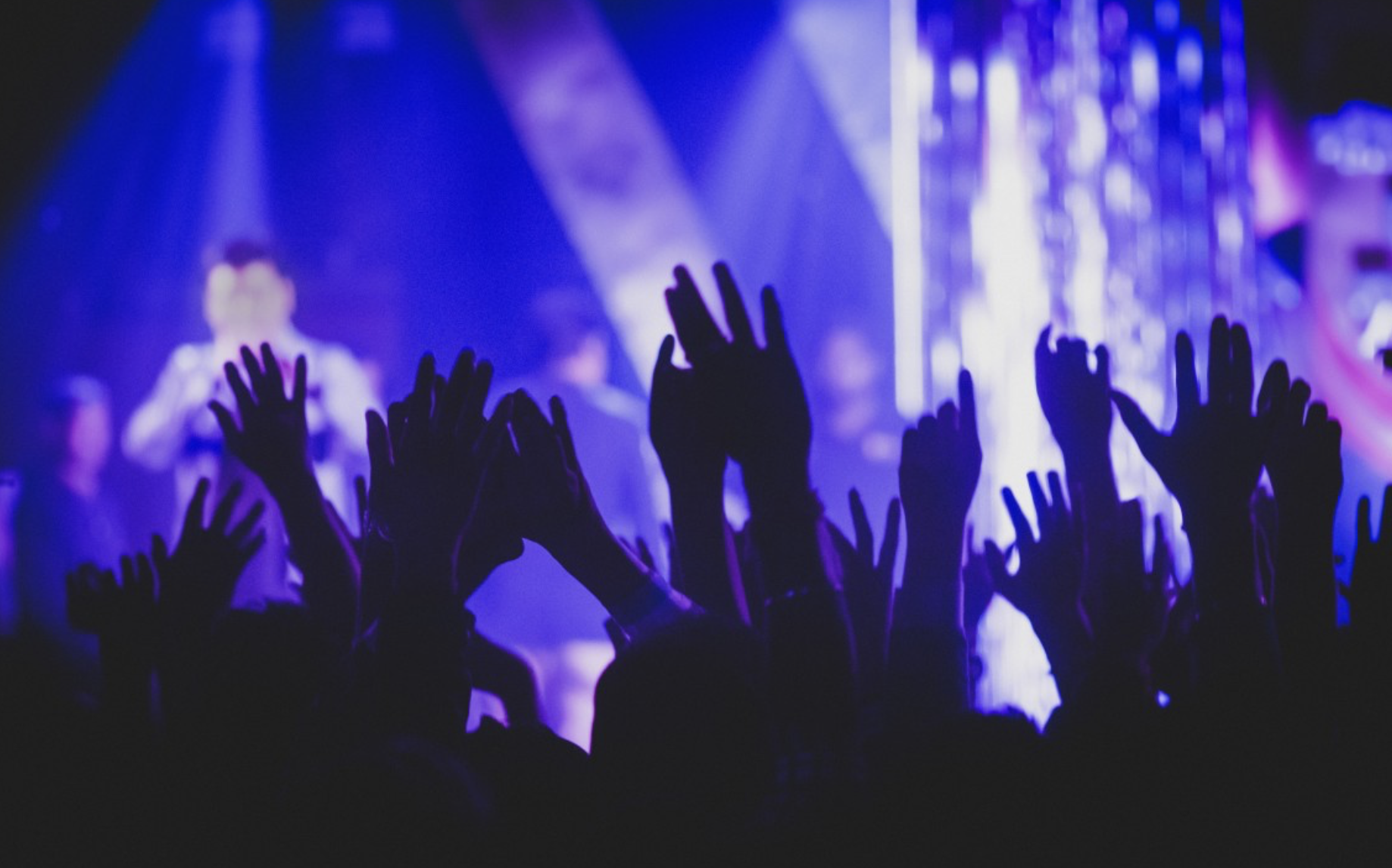 Stock image of concert goers hands in the air with purple lighting 